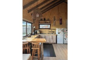 Una cocina rústica con vigas de madera, un lámpara colgante, una ventana y un refrigerador con imanes.