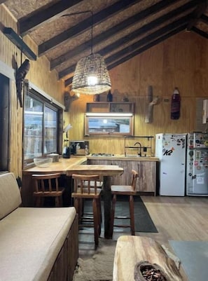 A cozy kitchen with wooden walls, a dining area with a bench, and a hanging light fixture. - Andean House (Malalcahuello)