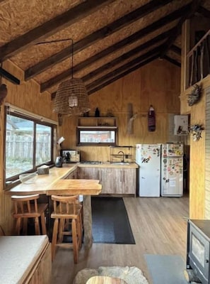 A rustic kitchen with wooden beams, a bar area, and a refrigerator with magnets. - Andean House (Malalcahuello)