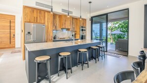 A modern kitchen with wooden cabinets, stainless steel appliances, and a large island with bar stools. - Family Getaway w/ Ocean & Valley Views in Guiones (Nosara)