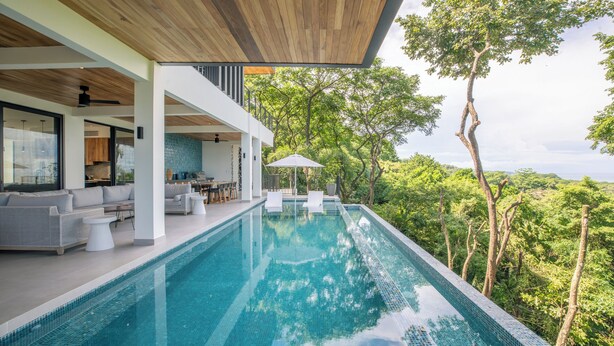 A modern infinity pool with a clear view of lush greenery and trees. - Family Getaway w/ Ocean & Valley Views in Guiones (Nosara)