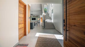 A modern interior with a wooden door, a staircase, and a kitchen area. - Family Getaway w/ Ocean & Valley Views in Guiones (Nosara)