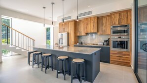 A modern kitchen with wooden cabinets, stainless steel appliances, and a central island with bar stools. - Family Getaway w/ Ocean & Valley Views in Guiones (Nosara)