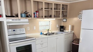 A kitchen with white cabinets, a stove, a sink, and a refrigerator. - Home Away From Home 2 (East Palatka)