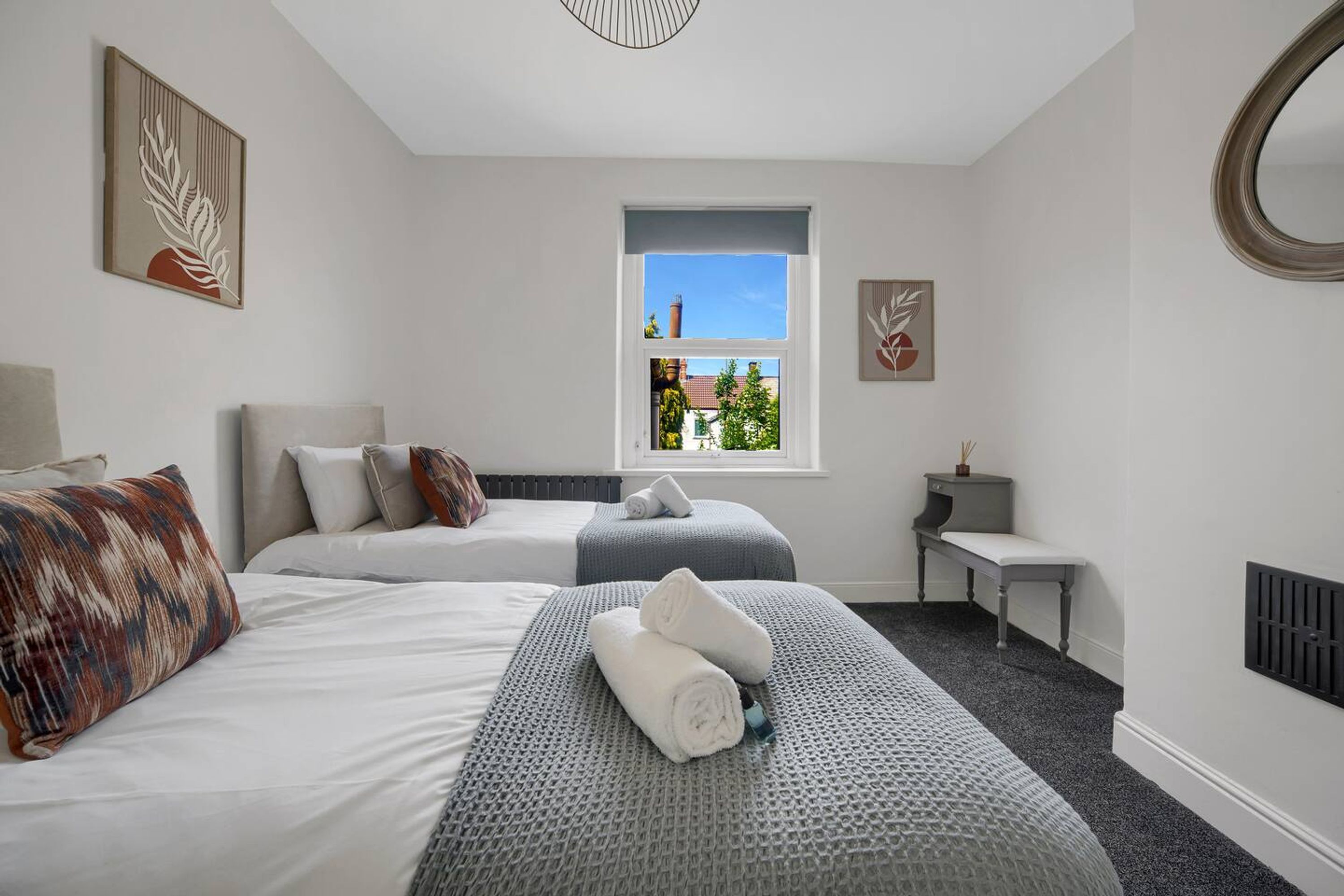 Hotellihuone, jossa on kaksi sänkyä, ikkuna, josta on näkymä, pieni pöytä ja penkki.