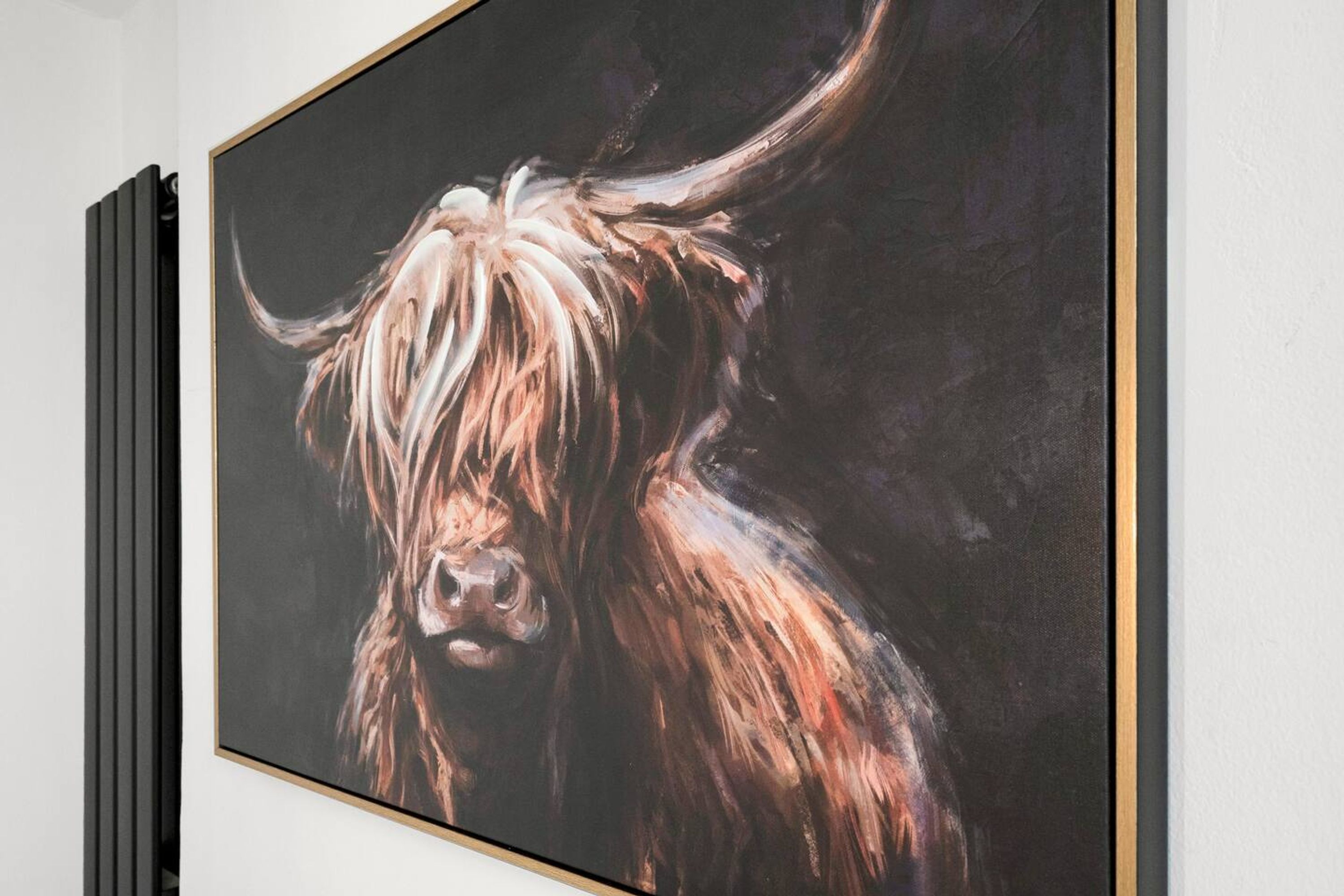 A framed painting of a yak on a white wall.