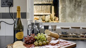 Een aanrecht met een fles Prosecco, verschillende soorten kaas, crackers, druiven, olijven en plakjes vlees. Ook staan er zout- en pepervaatjes, een broodje en een pot thee.