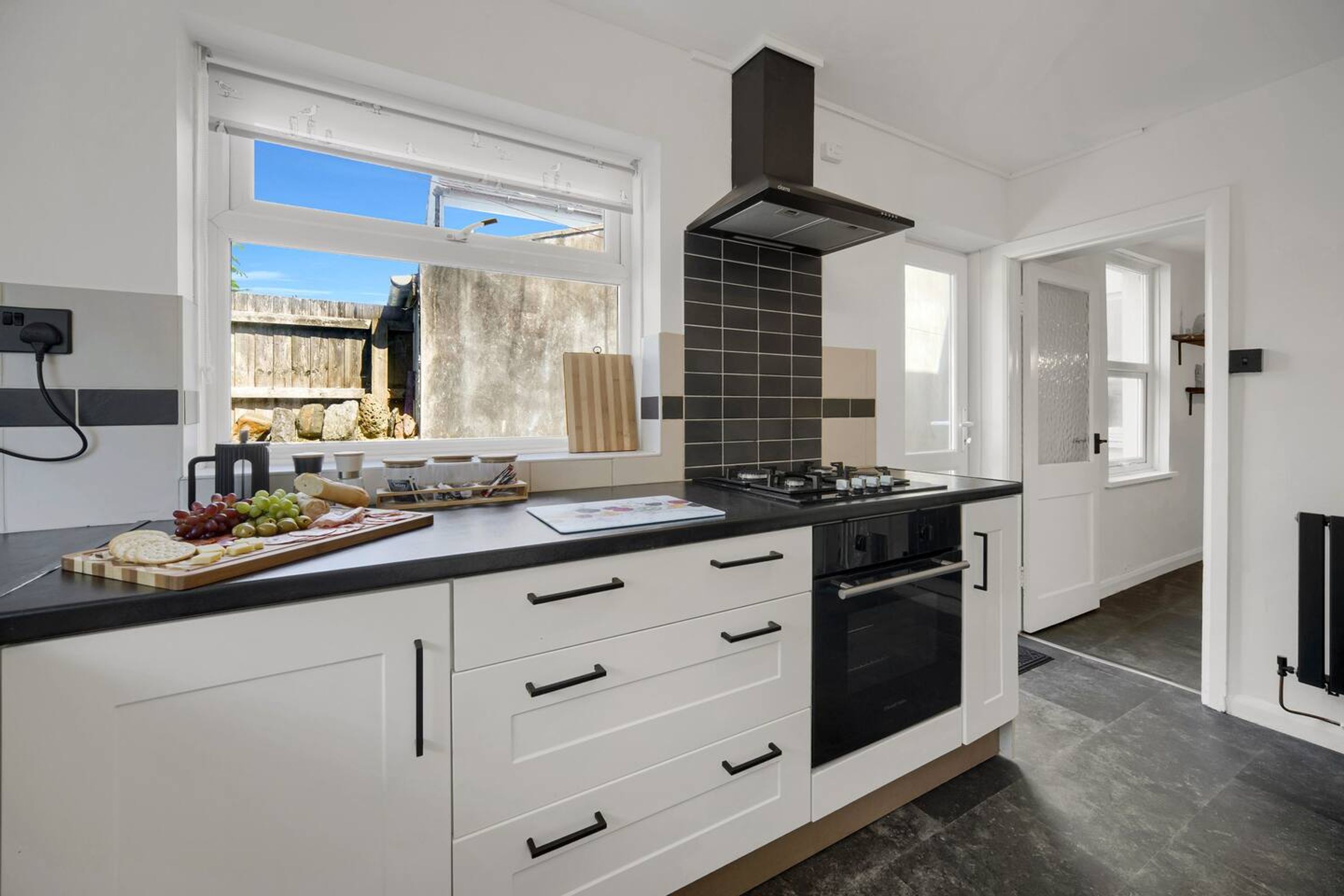 Una cucina moderna con una grande isola, piano cottura nero, mobili bianchi e una finestra che si affaccia su un giardino.