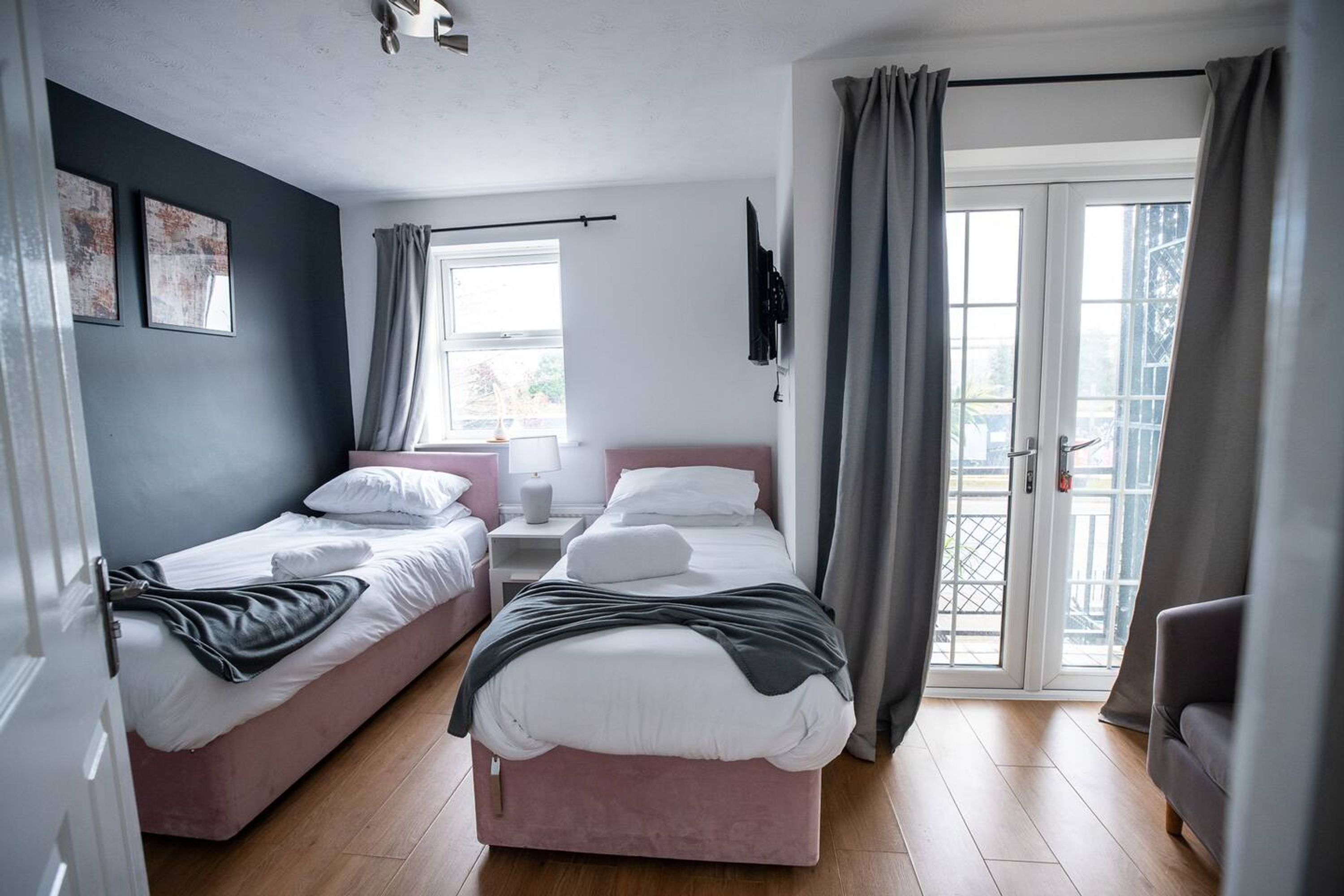 A bedroom with two beds, a TV, a window with curtains, and a balcony door.