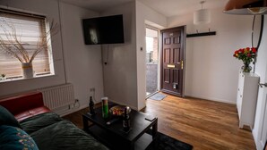 A living room with a sofa, a coffee table with a bowl and remote, a TV on the wall, and a door leading to a balcony. - Beautiful Cardiff Wharf Free Parking Waterviews (Cardiff)