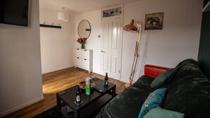 A living room with a dark green sofa, a small black coffee table with a bottle and a bowl, a red chair, a white door, and a wall-mounted TV. - Beautiful Cardiff Wharf Free Parking Waterviews (Cardiff)