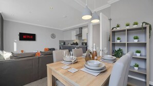 A modern living room with a dining area, a kitchen in the background, and a bookshelf with plants. - Spacious Cardiff Central Fast Wifi Netflix (Cardiff)