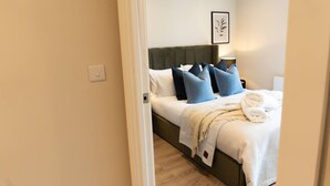 Ein ordentlich bezogenes Bett mit weißer und blauer Bettwäsche, einem Kopfteil und einem gerahmten Bild an der Wand.