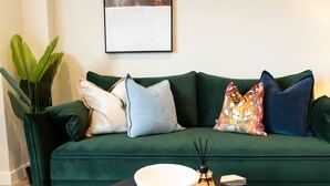 Ein grünes Sofa mit mehreren Kissen, eine weiße Schale und ein kleines dekoratives Objekt auf einem schwarzen Tisch.