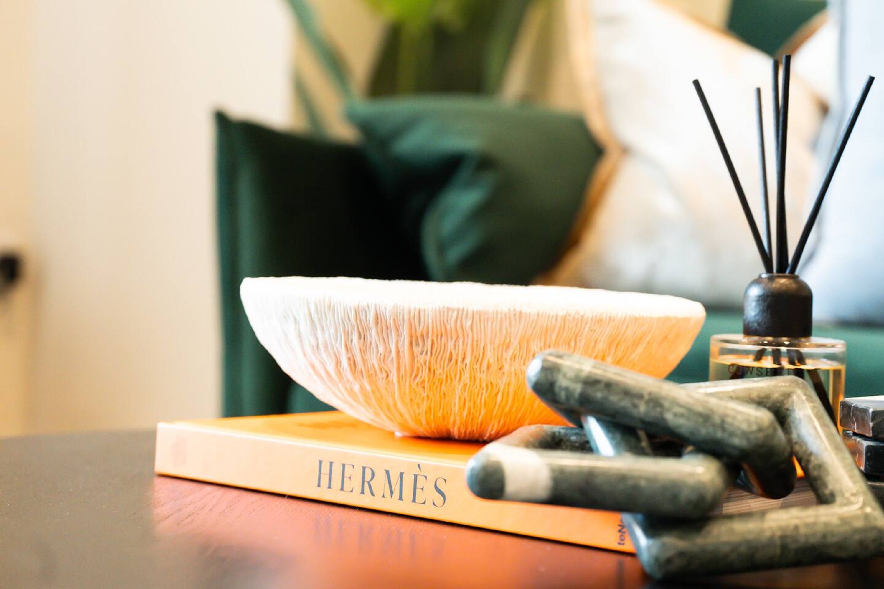 A book titled 'HERMÈS' on a table with a decorative bowl and a reed diffuser.