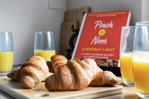 Croissants on a wooden board, two glasses of orange juice, and a cookbook titled "Pinch o' Nam Everyday Light". - Free Parking Fast Wifi 2 Min to Cardiff City (Cardiff)