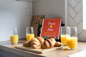 A kitchen counter with croissants, juice glasses, and a cookbook titled "Pinch of Nom Everyday Light". - Free Parking Fast Wifi 2 Min to Cardiff City (Cardiff)