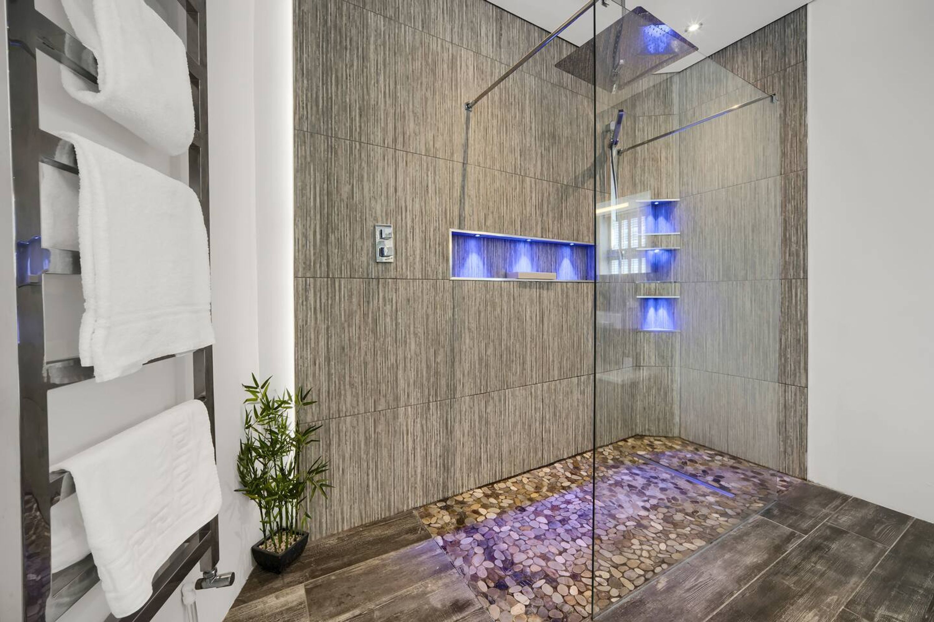 A modern bathroom with a glass-enclosed shower, wooden wall panels, and a pebble mosaic floor.
