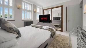 Moderni hotellihuone, jossa on suuri sänky, televisio, jossa näkyy Netflix, ja lasiovesta avautuva näkymä keittiöön.