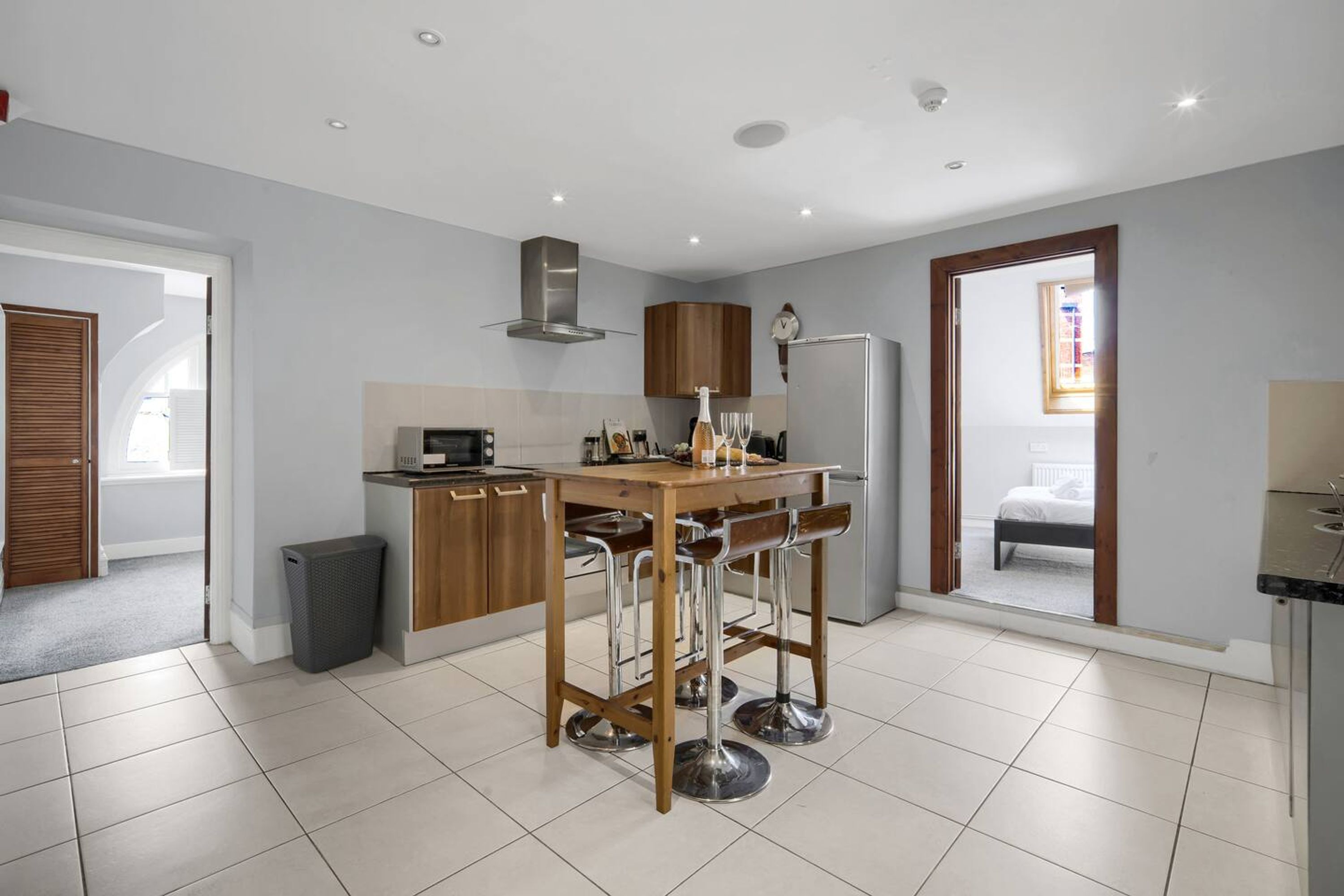 A modern kitchen with a central island, bar stools, a stainless steel range hood, and a refrigerator.