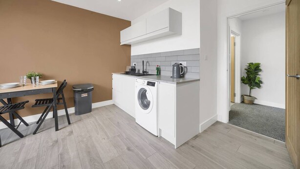 Une cuisine compacte comprenant un lave-linge, une table à manger avec des chaises et un petit plan de travail avec une bouilloire et une plante.