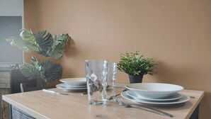 Une table à manger dressée avec des assiettes, un verre, des couverts et deux plantes en pot.