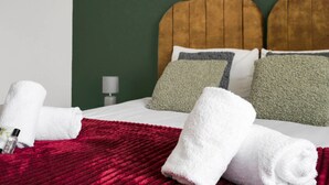 Un lit bien fait, avec des oreillers blancs et verts, une couverture rouge et des serviettes blanches pliées.
