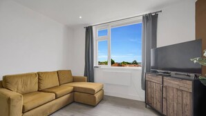 Un salon moderne avec un canapé, un téléviseur posé sur un meuble en bois et une grande fenêtre avec des rideaux.