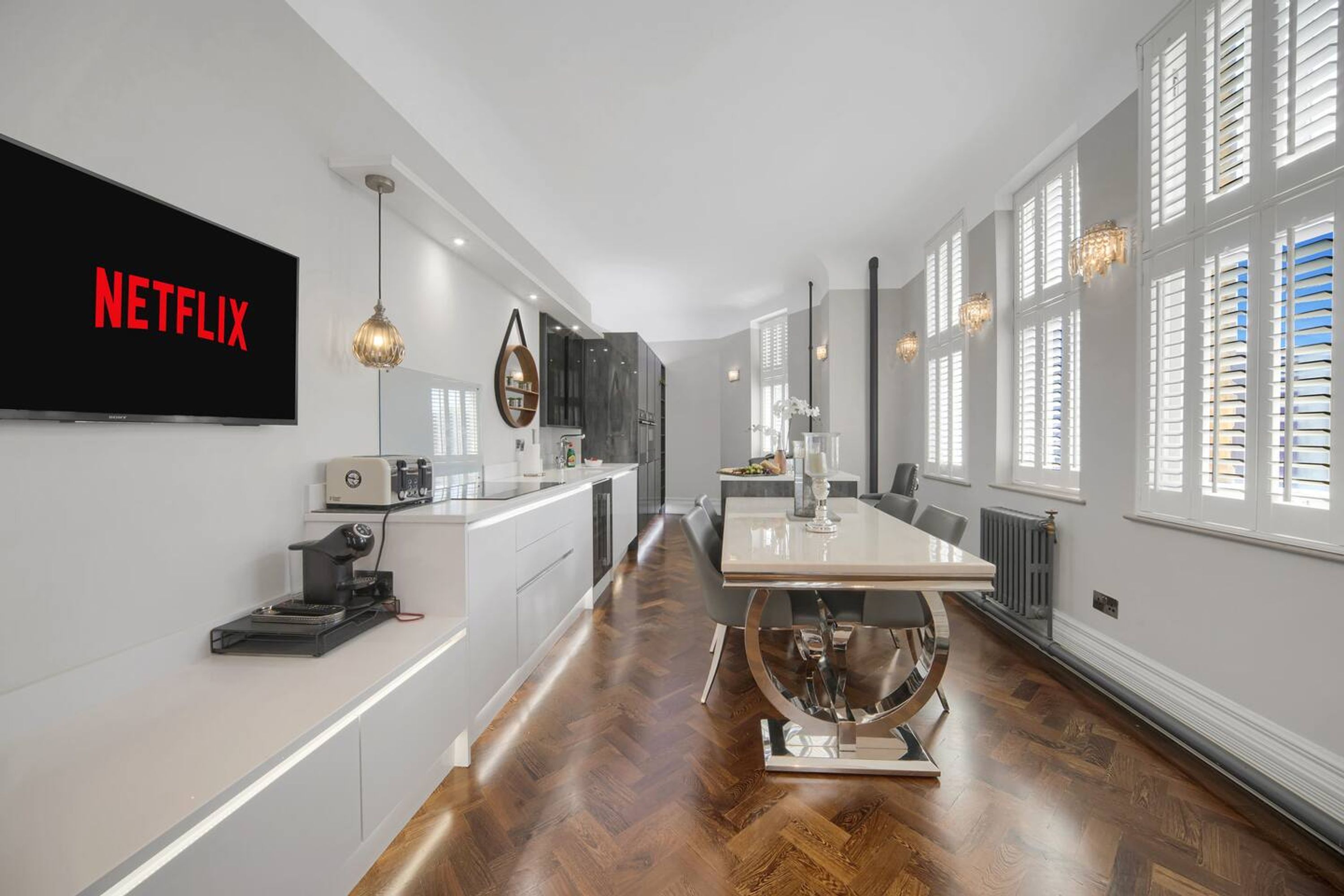 A modern kitchen with a built-in oven, a coffee machine, and a large flat-screen TV displaying 'NETFLIX'.