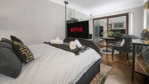 A modern hotel room with a large bed, a flat-screen TV displaying 'NETFLIX', a small table with chairs, and a mirror reflecting the room. - Modern Unique - Central Beach Access (Swansea)