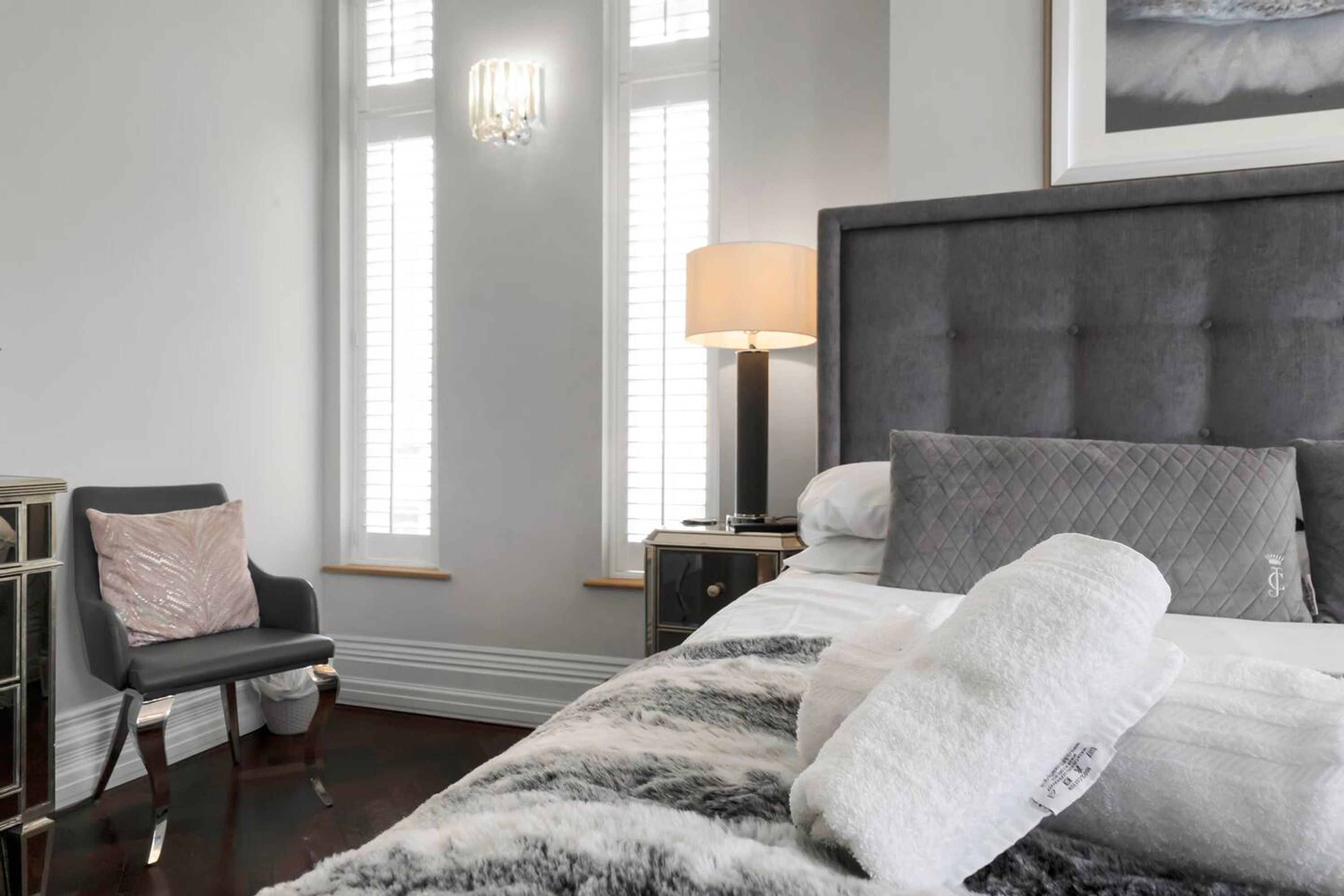 Un dormitorio ordenado con una cama grande, una silla, una mesita de noche y una lámpara.
