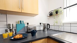 A modern kitchen with wooden cabinets, a black countertop, a toaster, a kettle, and a hanging plant. - Central Escape Central Cardiff Free Parking (Cardiff)