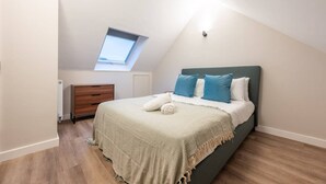 A bedroom with a sloped ceiling, a skylight, a bed with a green headboard, and a wooden dresser. - Luxurious 2 Bed Central Cardiff Free EV Charge (Cardiff)