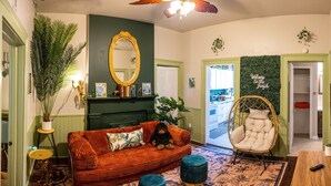A cozy living room with a sofa, a chair, a mirror, and a green wall with a 'Welcome to the Jungle' sign. - The Jungle Nook: Themed,Steps to Forsyth,King Bed,Grill,Games,Picnic Basket (Savannah)