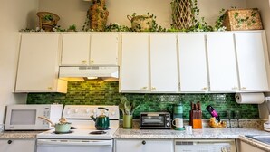 A kitchen with white cabinets, a green tiled backsplash, a microwave, a stove, a toaster, and various kitchen utensils. - The Jungle Nook: Themed,Steps to Forsyth,King Bed,Grill,Games,Picnic Basket (Savannah)