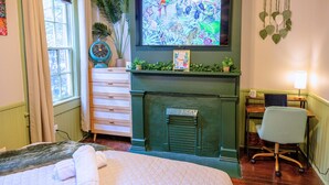 A room with a bed, a desk, a chair, a fireplace, a TV, and a window with curtains. - The Jungle Nook: Themed,Steps to Forsyth,King Bed,Grill,Games,Picnic Basket (Savannah)
