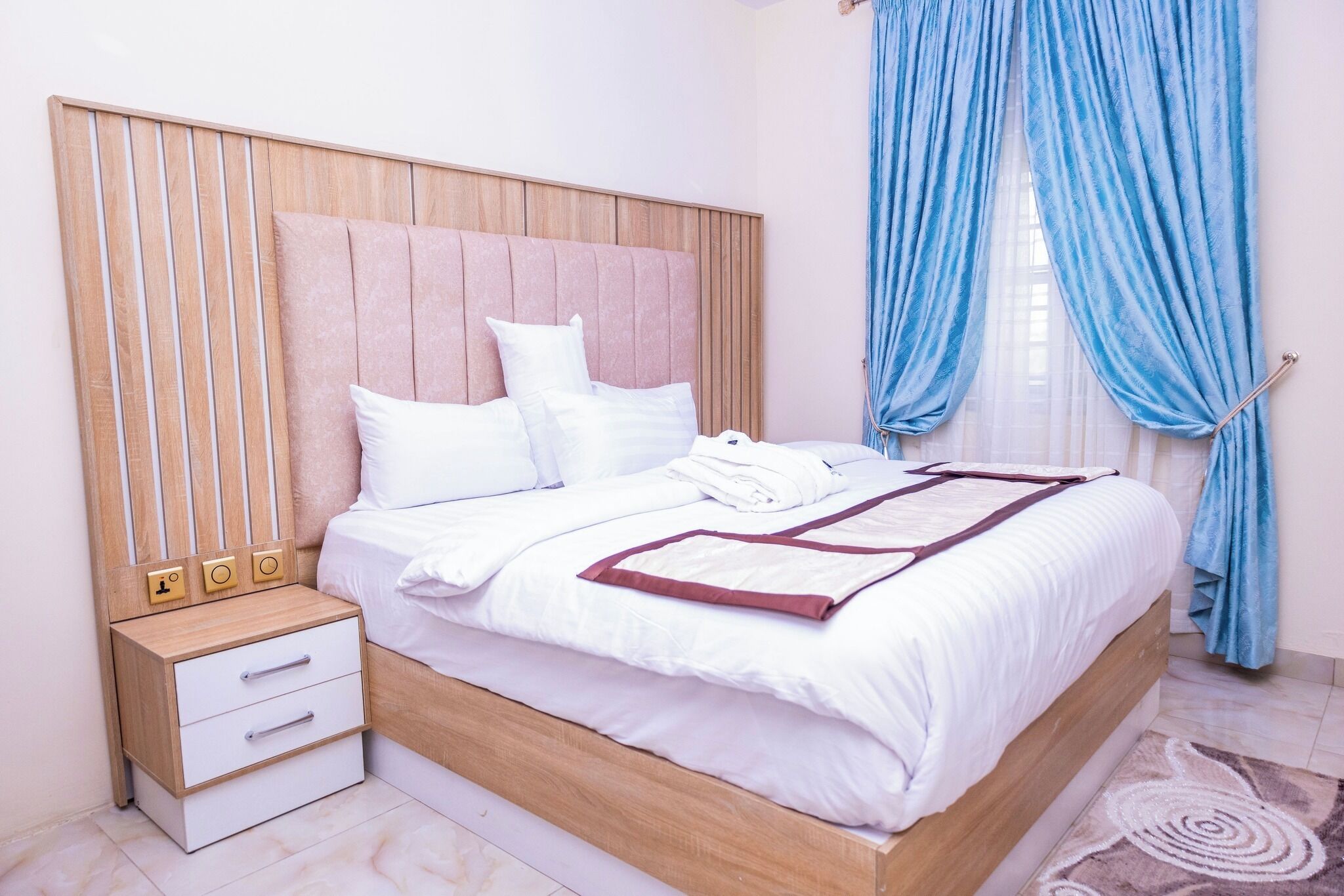 Una cama bien hecha con sábanas blancas, cabecero de madera y mesita de noche con cajones.