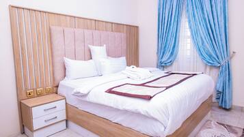 Una cama bien hecha con sábanas blancas, cabecero de madera y mesita de noche con cajones.