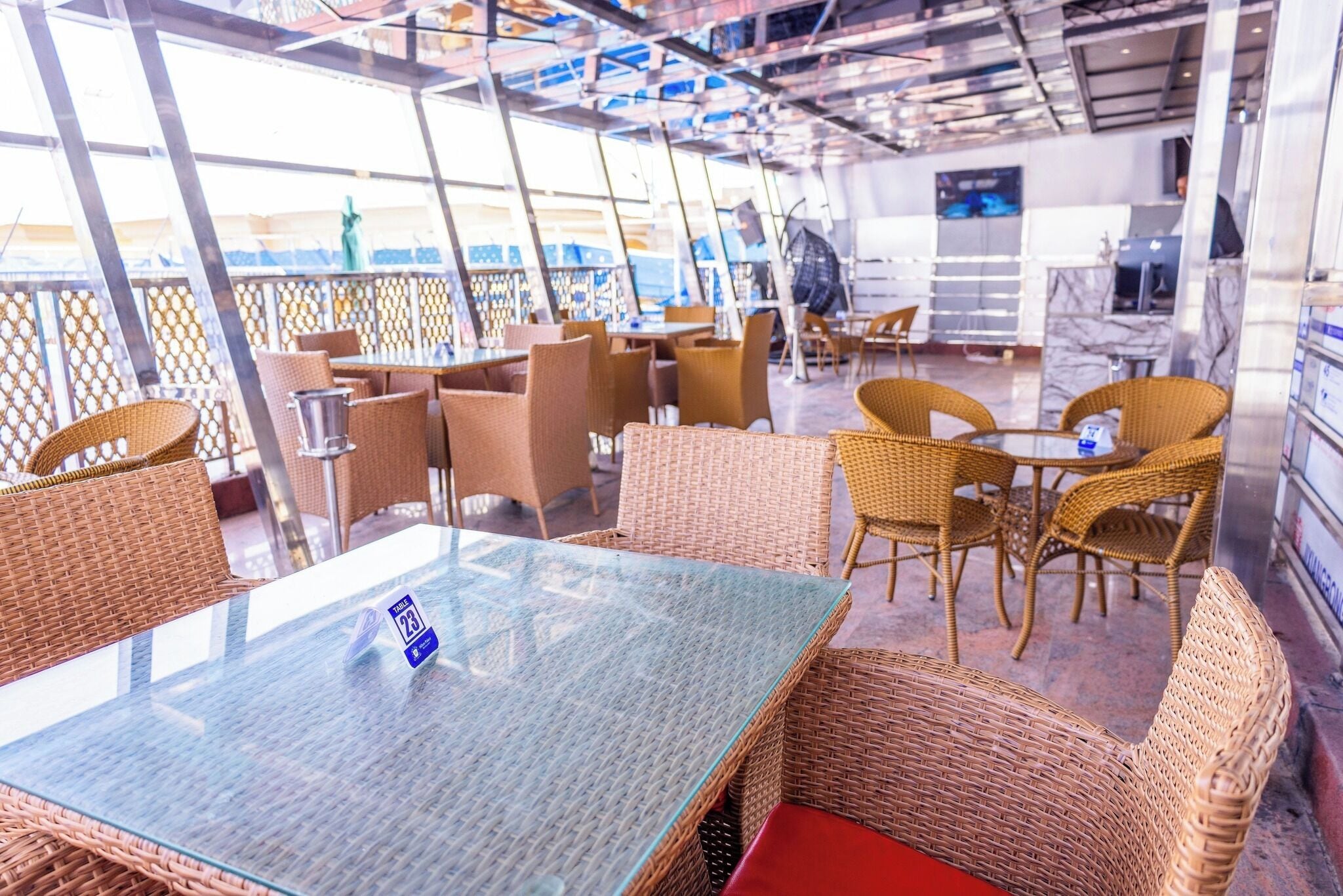 A restaurant with wicker furniture, glass tables, and a view of the sea.
