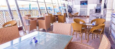A restaurant with wicker furniture, glass tables, and a view of the sea.