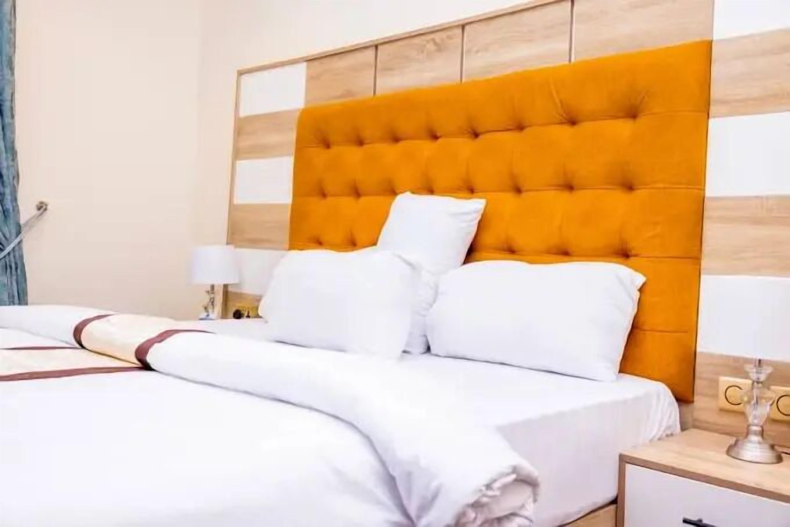Una cama con ropa de cama blanca y un cabecero naranja con botonadura.