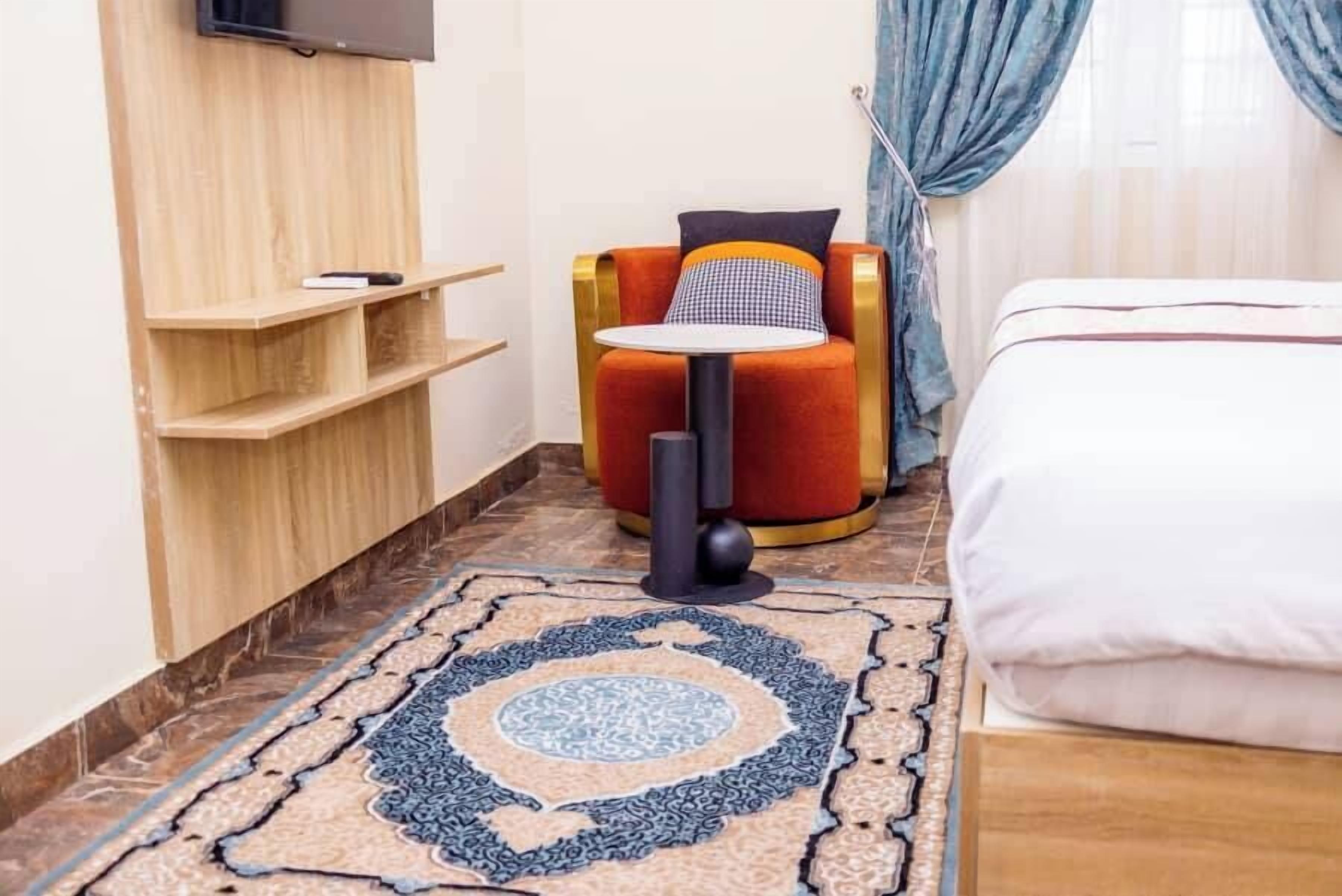 A hotel room with a bed, a small table with a chair, a TV mounted on the wall, and a patterned rug.