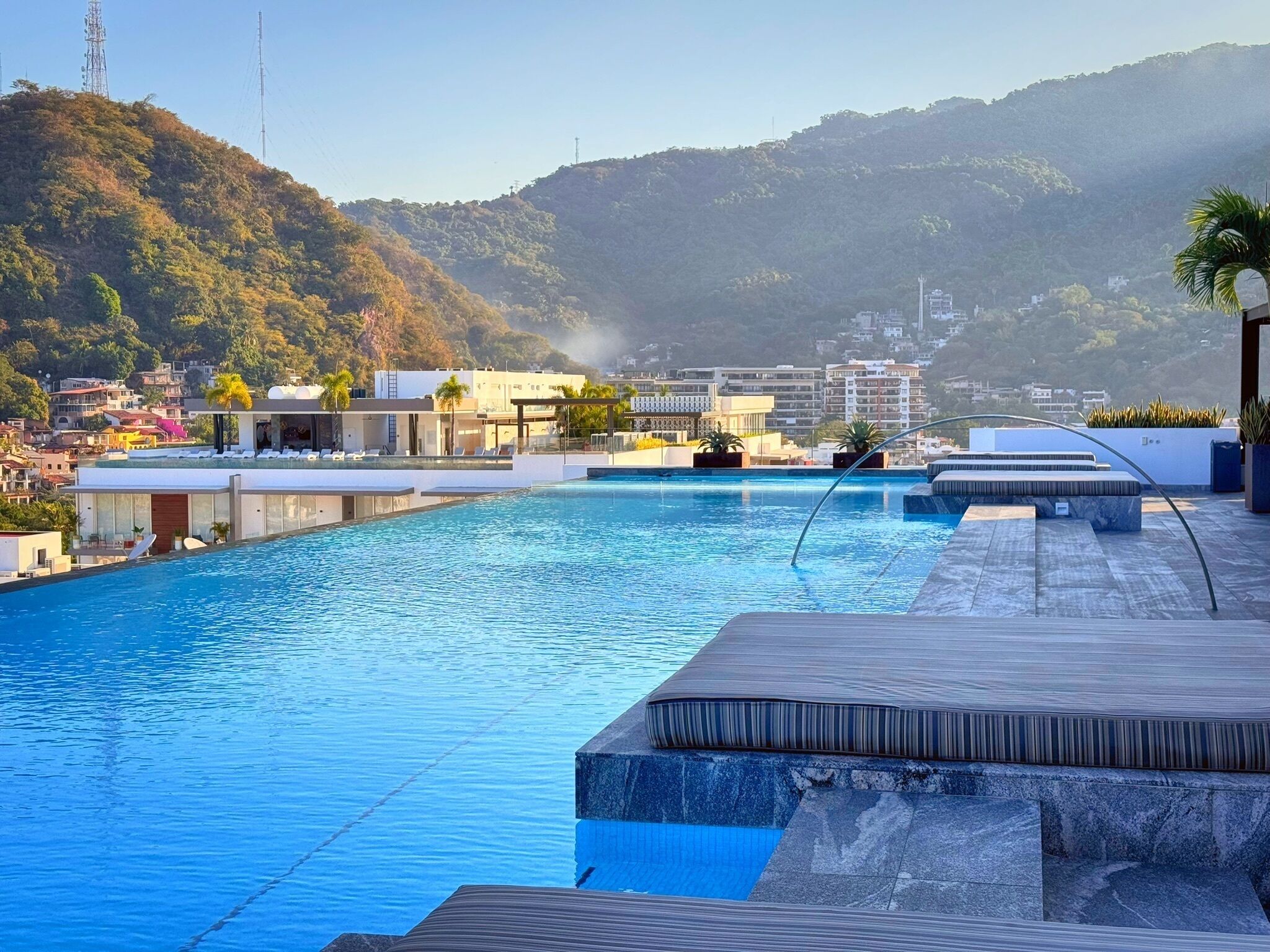 A rooftop infinity pool with a view of a hillside and buildings in the background.