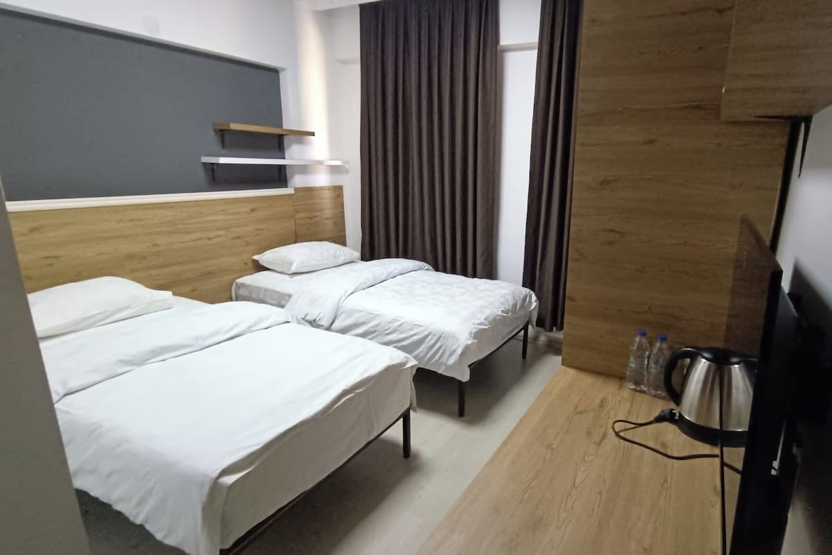 A hotel room with two single beds, a wooden headboard, a flat-screen TV, and a kettle.