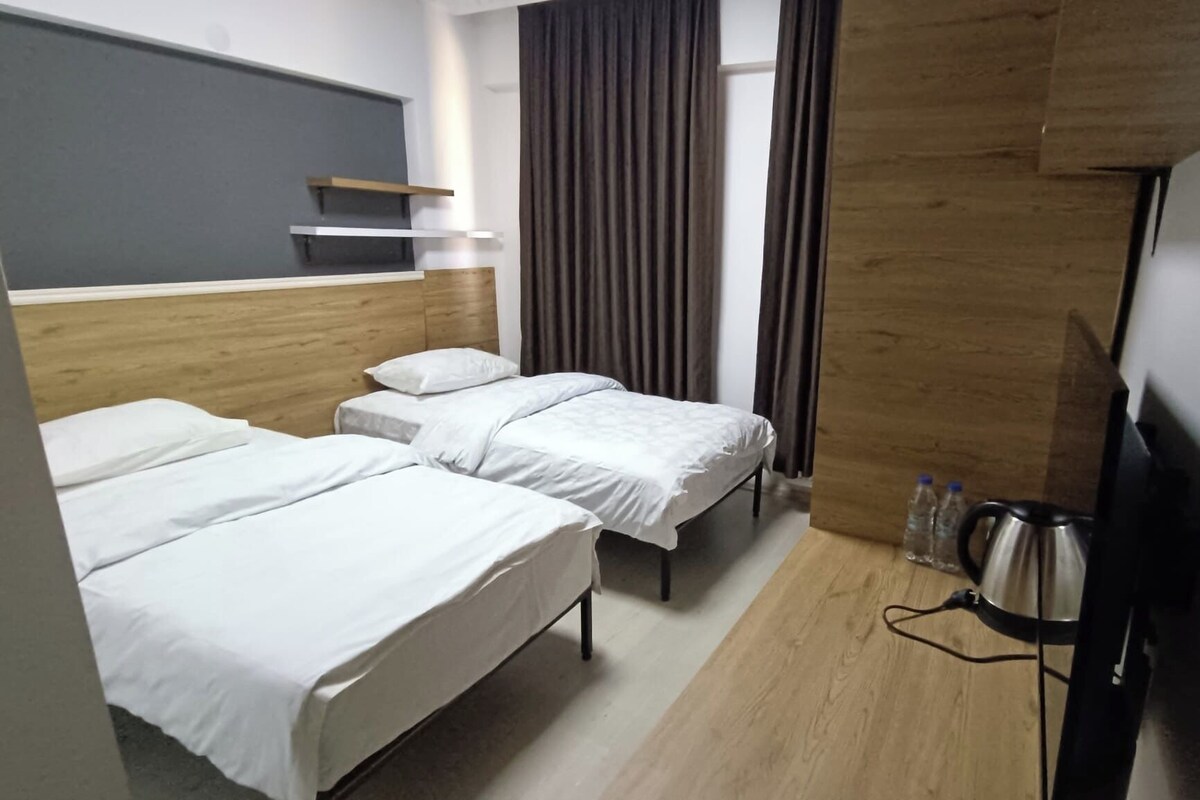 A hotel room with two single beds, a wooden headboard, a flat-screen TV, and a kettle.