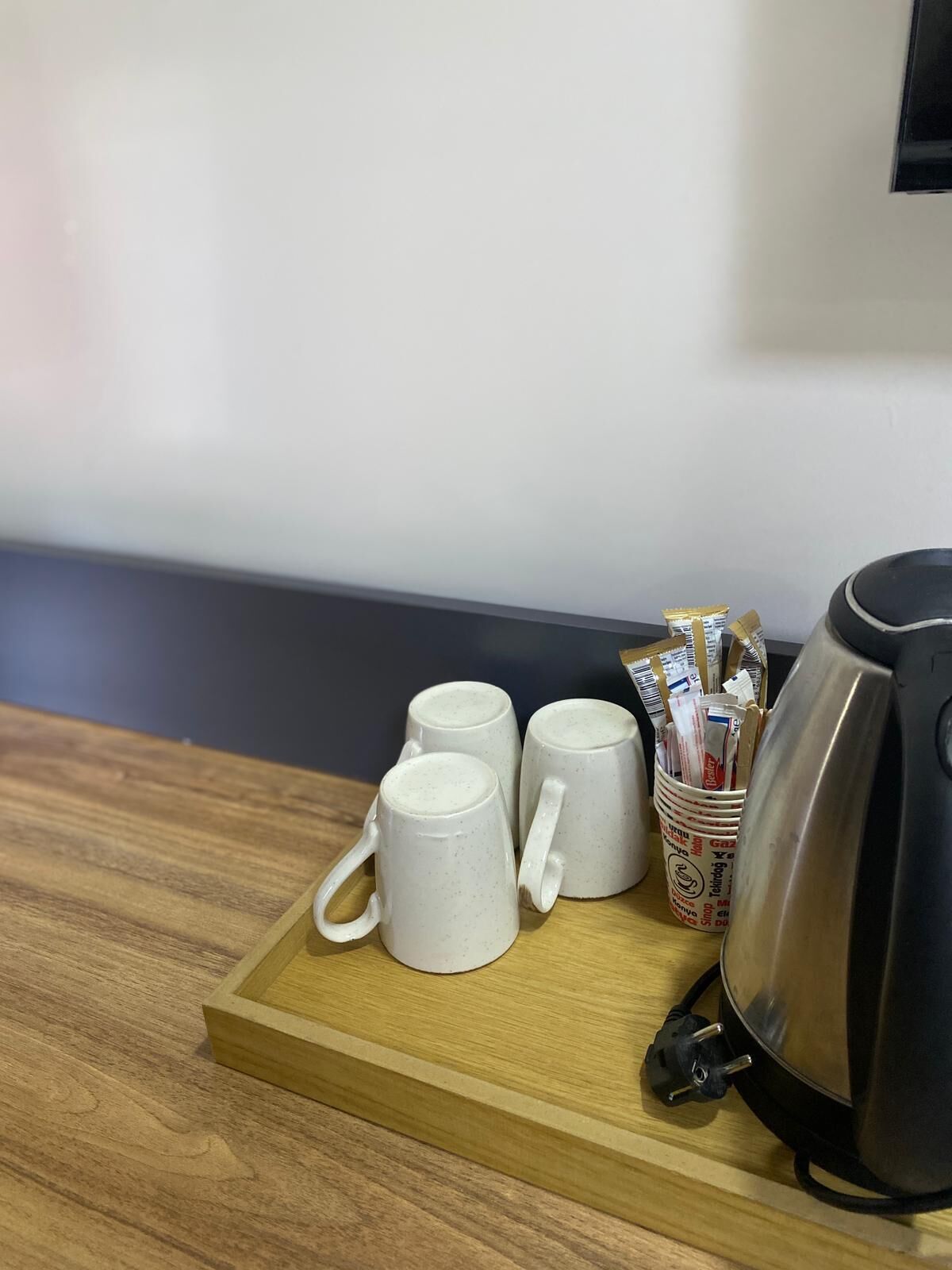 A wooden tray with three white mugs and a kettle on a table.