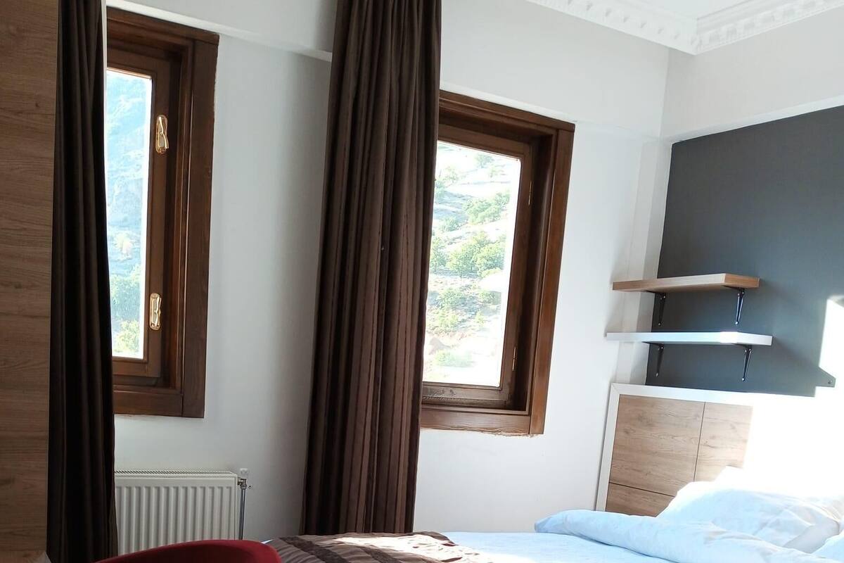 A modern bedroom with a wooden bed, a red chair, and two windows with curtains.