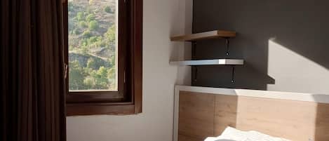 Een hotelkamer met een bed, een raam met gordijnen, een hoofdeinde en een plank.