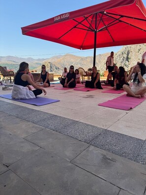 A group of people sitting on yoga mats under a red umbrella in an outdoor setting with a mountainous backdrop. - SERGE HOTEL  (Arapgir)