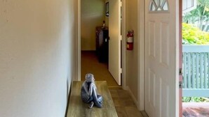A hallway with a bench, a door leading outside, and a fire extinguisher on the wall. - Heavenly Kauai Destinations Hale Moi Side B by Hideaways Beach (Princeville)